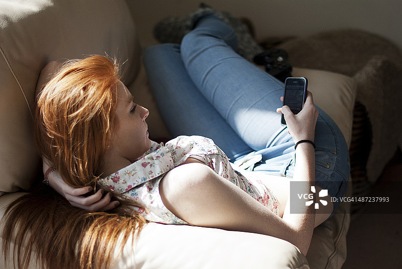 躺在扶手椅上使用手机的少女图片素材