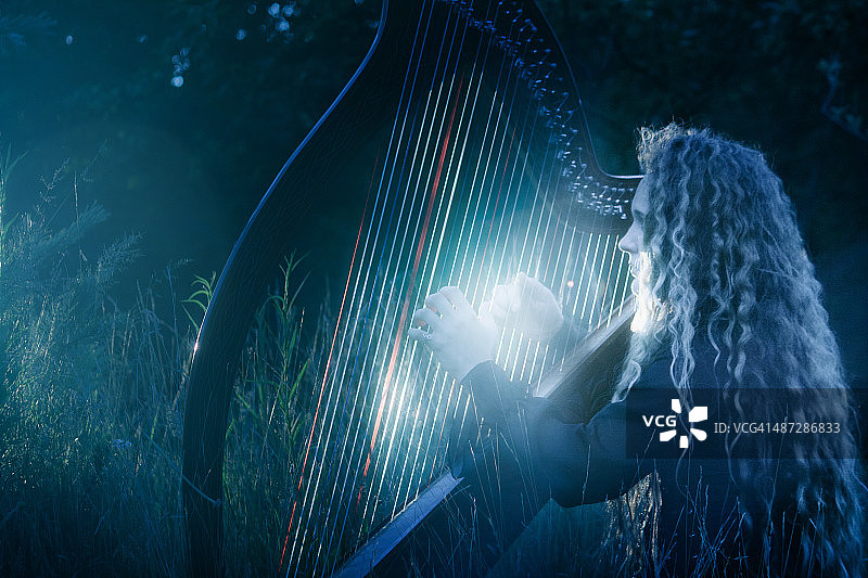 年轻女子夜晚在户外演奏凯尔特竖琴图片素材