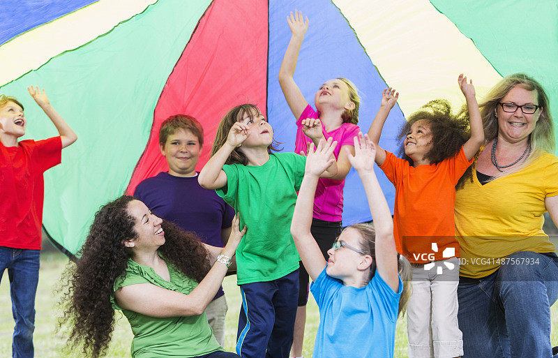 孩子们在彩色降落伞下与营地辅导员一起玩耍图片素材