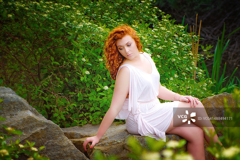 坐在公园里的白人红发女子，眼神向下看图片素材