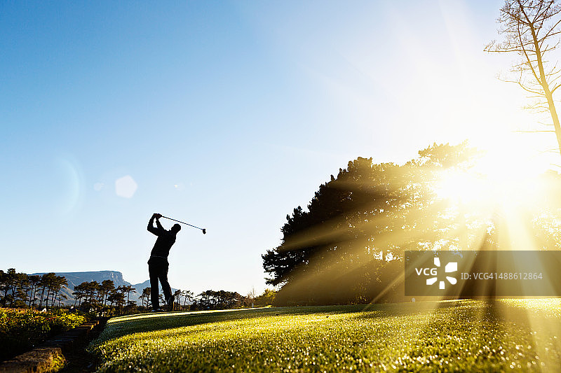 在美丽的阳光球场上挥杆的年轻高尔夫球手图片素材