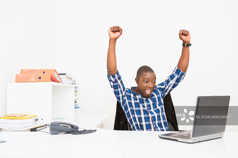 在南非豪登省约翰内斯堡，商务人士看着笔记本电脑屏幕，高兴地举起双手图片素材