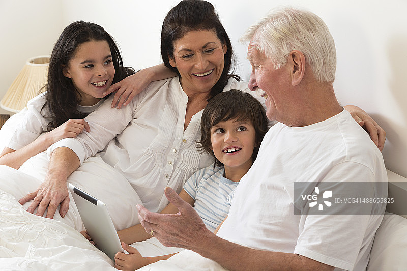 祖父母和孙辈在床上使用平板电脑图片素材