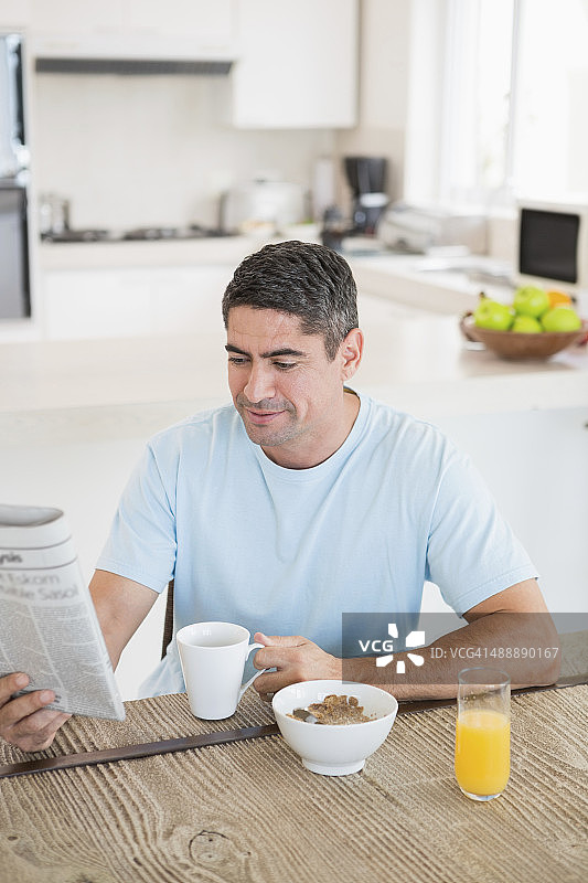 男子在厨房里边看报纸边喝咖啡图片素材