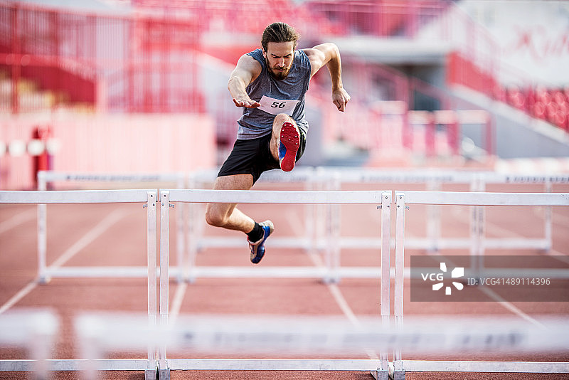 年轻的运动男人努力跳跃跨栏图片素材