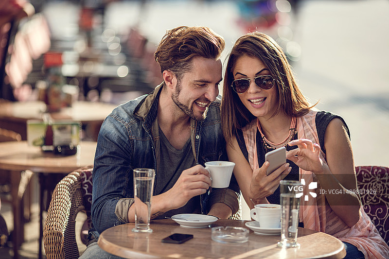 微笑情侣在咖啡馆放松并使用智能手机图片素材