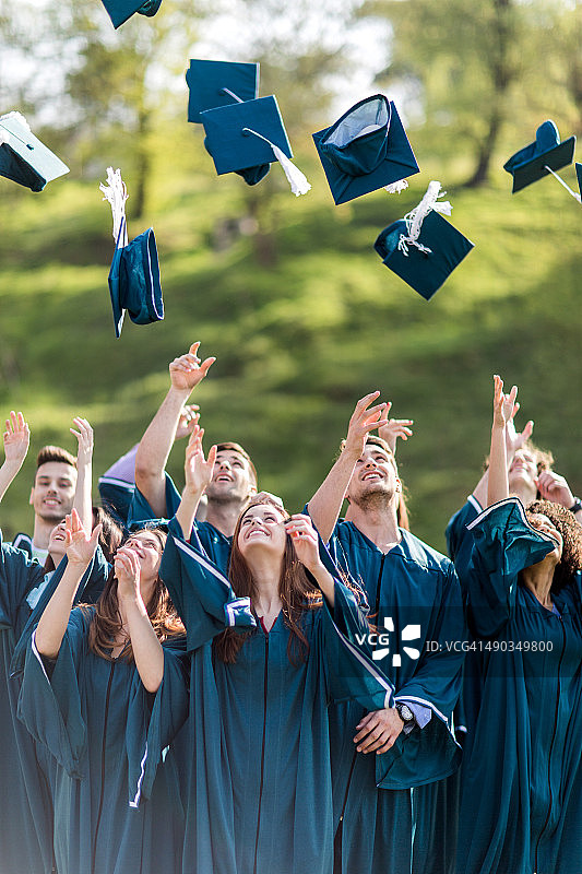 快乐的毕业学生将学士帽抛向空中图片素材