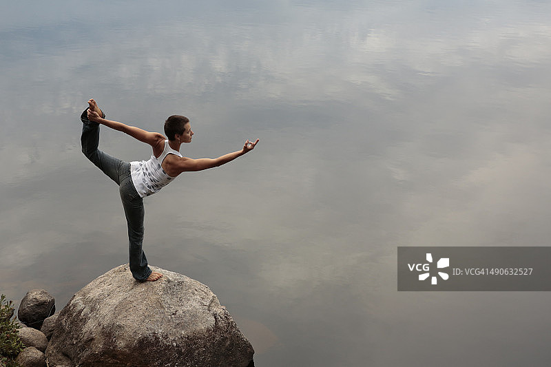 宁静水边岩石上练习瑜伽的女人图片素材