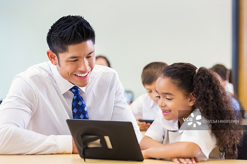 可爱的小学年龄女孩和老师一起使用数位板图片素材