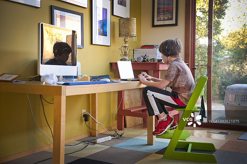 在客厅电脑桌旁使用笔记本电脑的男孩图片素材