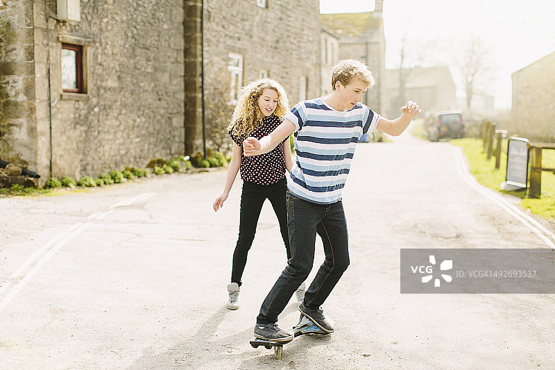 青少年兄妹在乡间小路上玩滑板图片素材