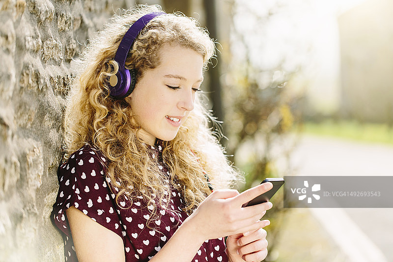 在村庄里戴着耳机和智能手机的少女肖像图片素材