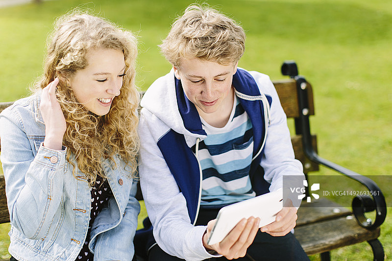 在长凳上看平板电脑的青少年兄妹图片素材