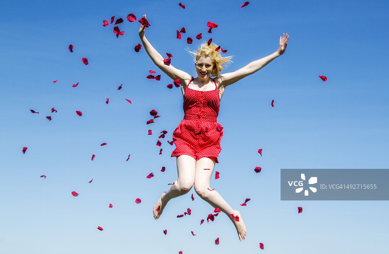 在空中跳跃，周围散落着玫瑰花瓣的女子肖像图片素材