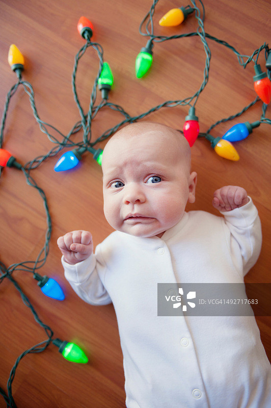 宝宝躺在地板上，周围是圣诞灯饰图片素材