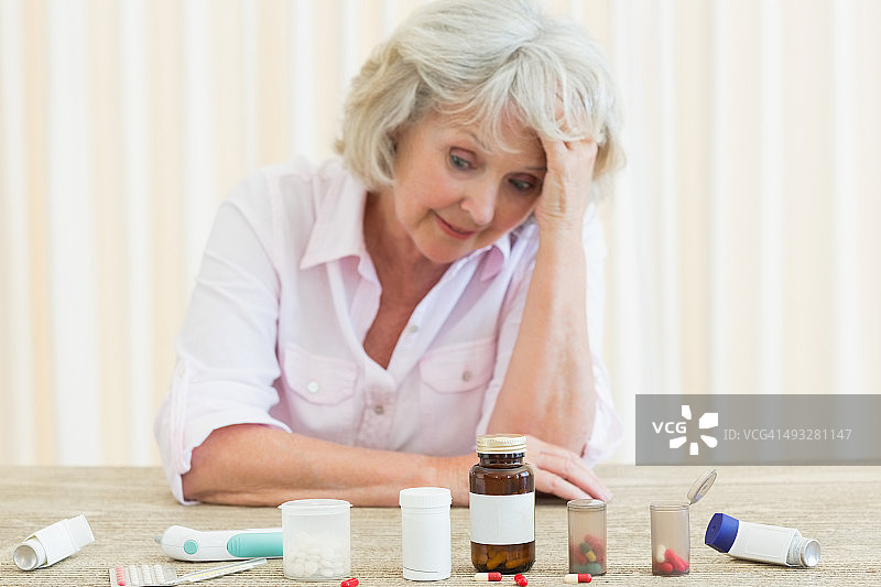 桌子上放着各种药丸，感到困惑的老年妇女图片素材