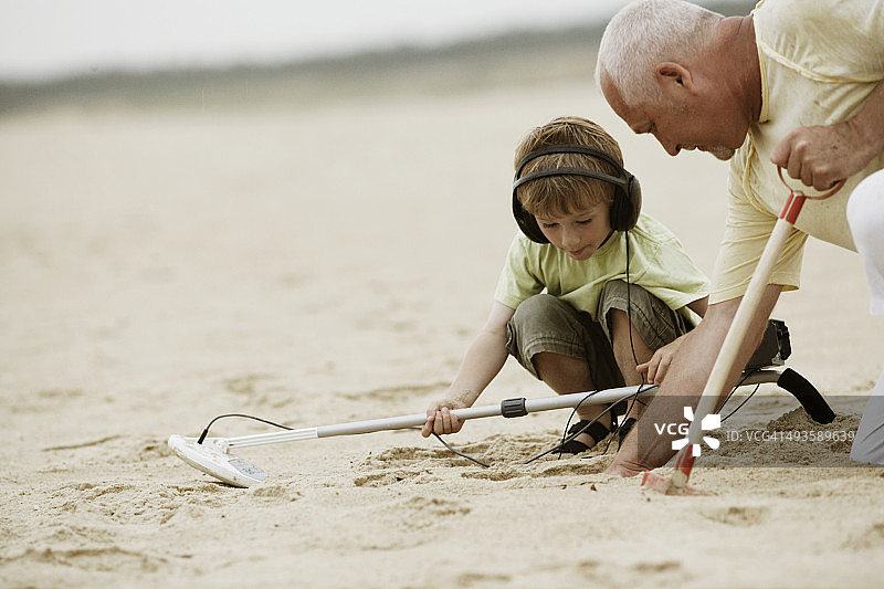 男人和男孩带着金属探测器和铲子在海滩上图片素材
