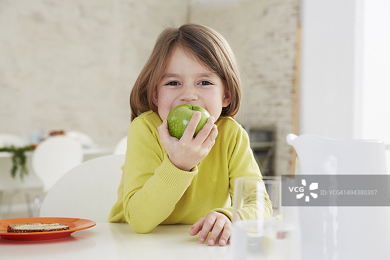 德国慕尼黑：女孩坐在桌旁，拿着绿苹果图片素材