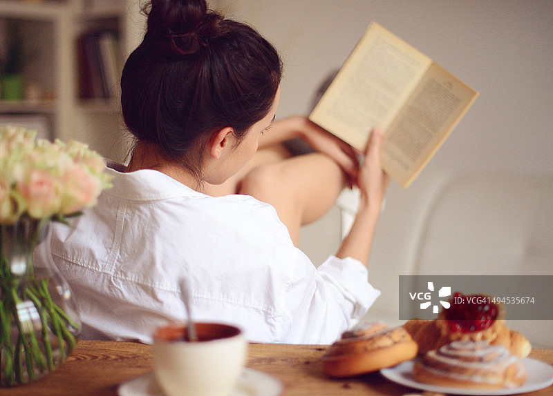 年轻女人一边吃早餐一边看书图片素材