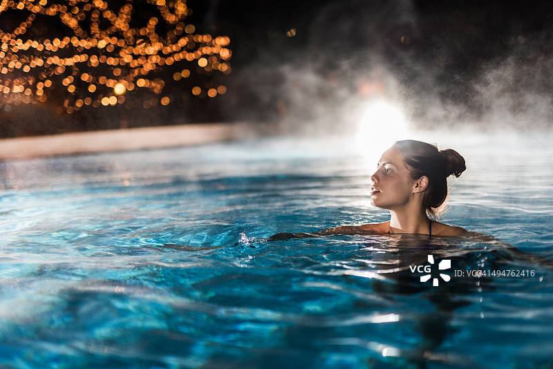 夜晚在恒温泳池中享受的年轻女人图片素材
