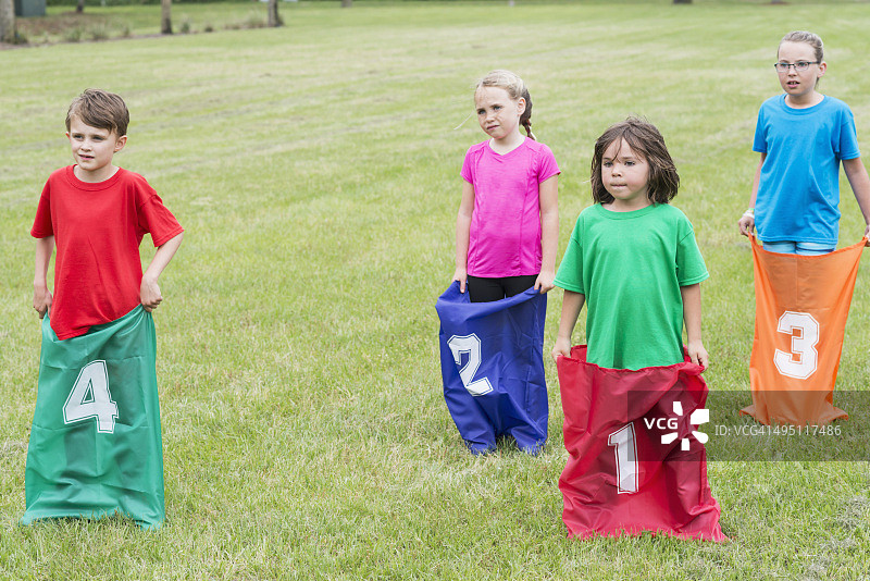 四个孩子准备好参加麻袋赛跑图片素材