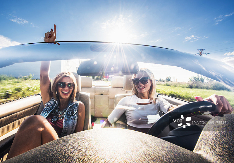 在阳光明媚的日子里驾驶敞篷车的年轻快乐女人们图片素材