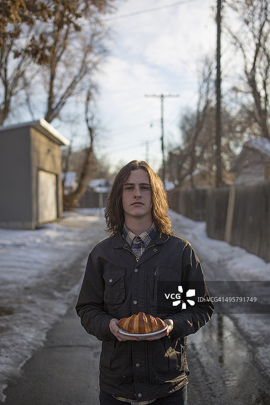 男孩在小巷里拿着一个羊角面包图片素材