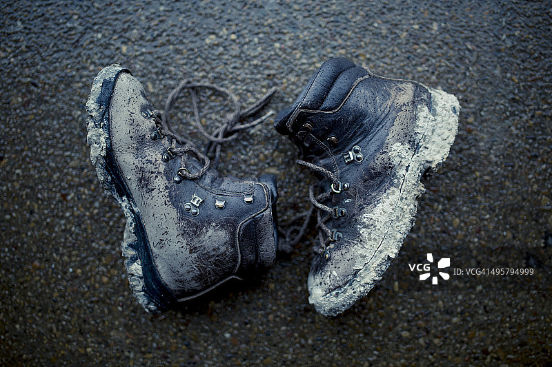 一双沾满泥土的登山靴放在水泥地上。图片素材