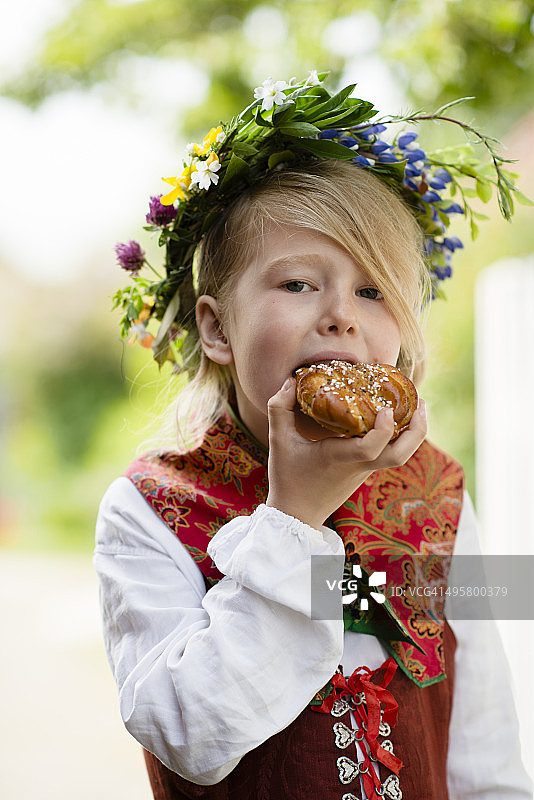穿着民族服装吃肉桂卷的女孩，瑞典桑德哈姆图片素材