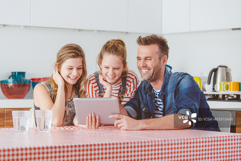 父亲在厨房里和女儿们一起使用平板电脑图片素材
