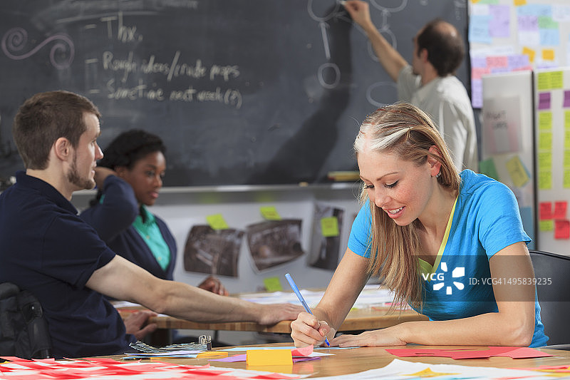 工程学讲师在黑板上制作流程图，学生们在做项目，一位脊髓损伤，另一位患有阿斯伯格综合征图片素材