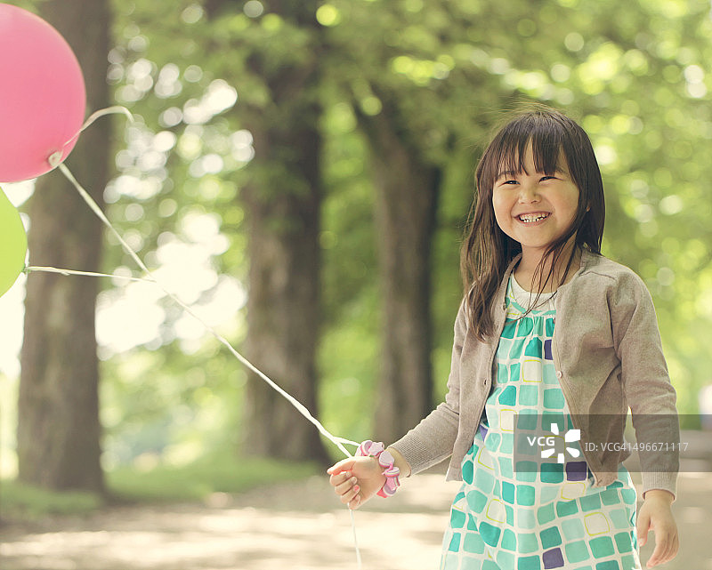 在公园里带着气球、笑容灿烂的年轻女孩图片素材