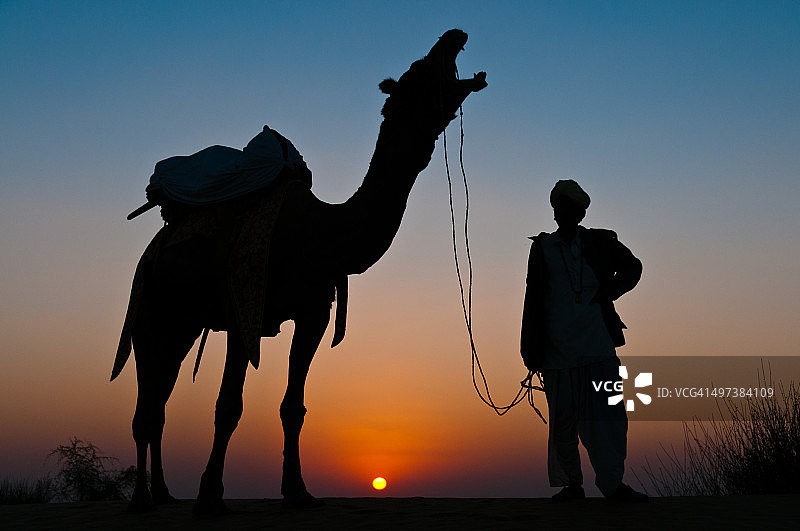 沙漠日落时分的骆驼与驯兽师图片素材