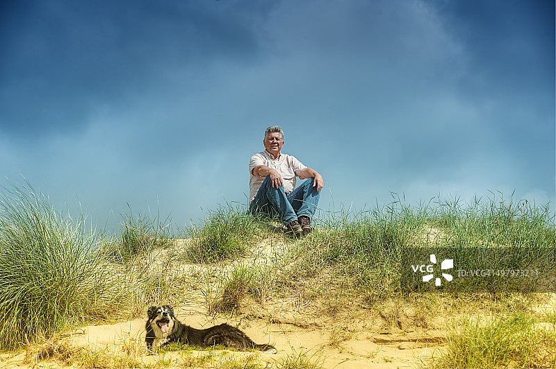 男人和狗坐在沙丘上图片素材