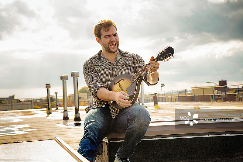 年轻男人在布鲁克林屋顶弹曼陀林图片素材