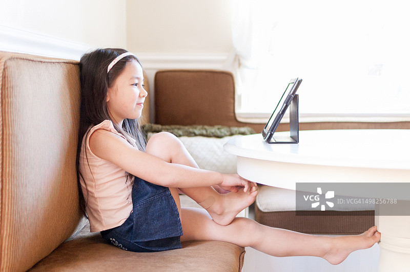 快乐的小女孩坐在厨房的桌子旁使用平板电脑图片素材