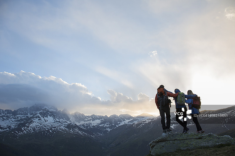 三名徒步者在山顶岩石上互相搀扶图片素材