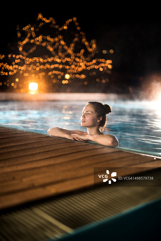 冬天夜晚在加热游泳池中放松的年轻女人图片素材