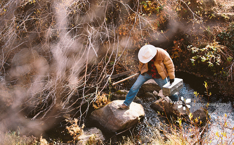 男人携带工具，踩着石头过河图片素材