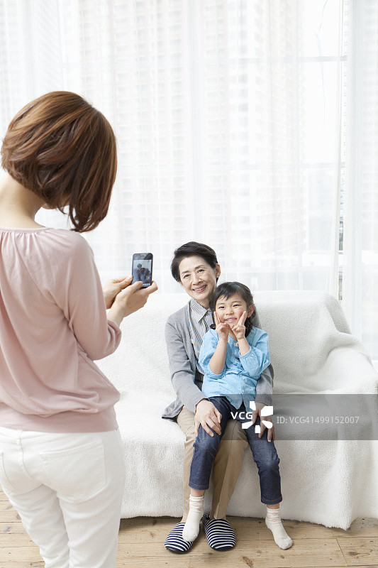 60岁的祖母和20岁的母亲以及坐在沙发上的5-9岁女儿图片素材