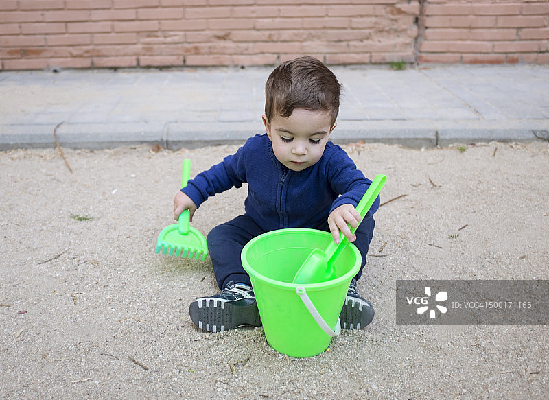 男孩玩沙桶、耙子和绿色铲子图片素材