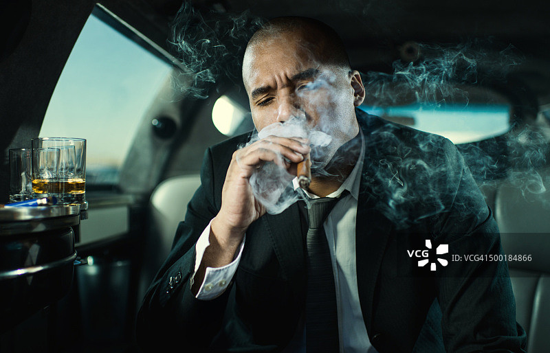 坐在豪华轿车里抽雪茄的非裔美国商人图片素材