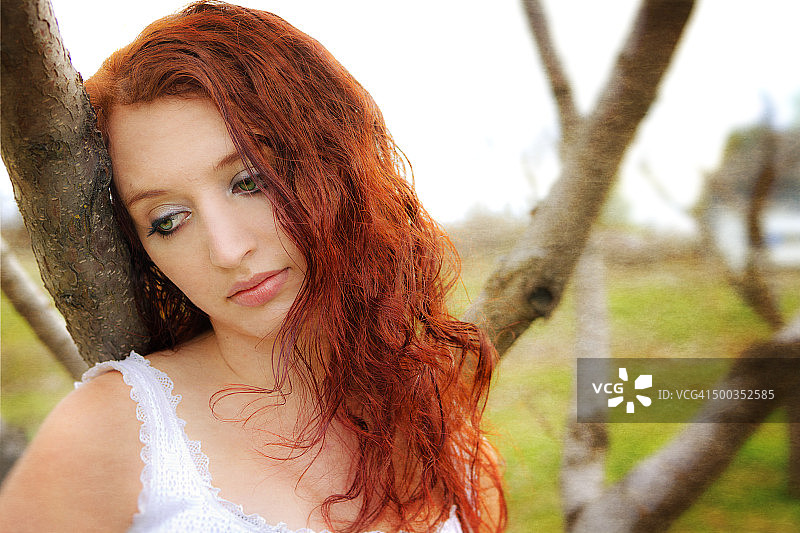 早春时节倚靠在树旁的红发人图片素材