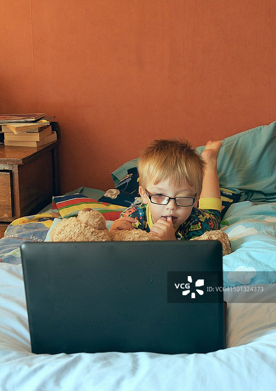 小男孩在床上使用笔记本电脑图片素材