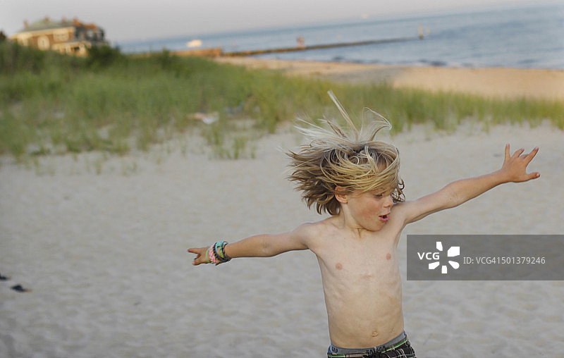 男孩在沙滩上从栏杆跳下图片素材