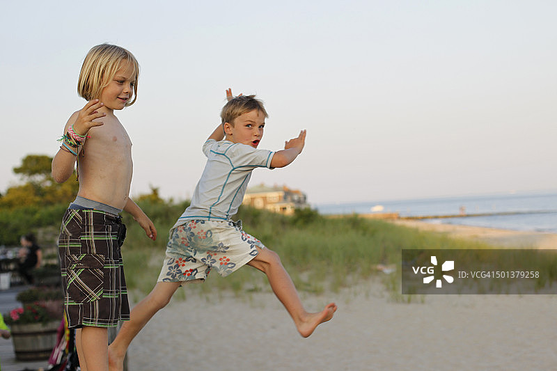 男孩在沙滩上从栏杆跳下图片素材