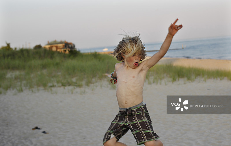 男孩在沙滩上从栏杆跳下图片素材