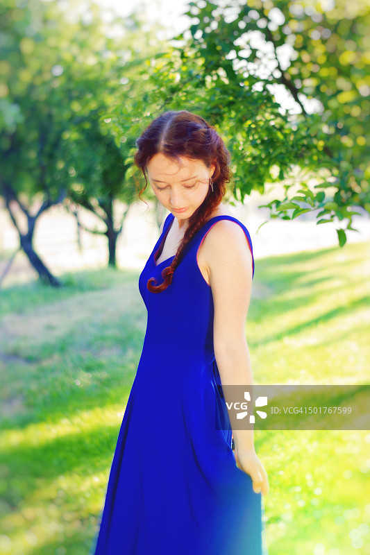 穿蓝色连衣裙的年轻红发女子在果园里图片素材