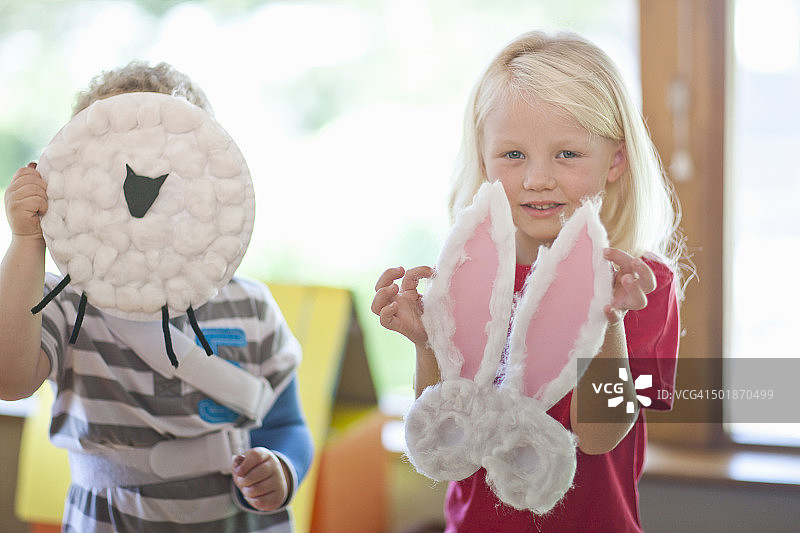 幼儿园里，男孩和女孩举着绵羊和兔子作品图片素材