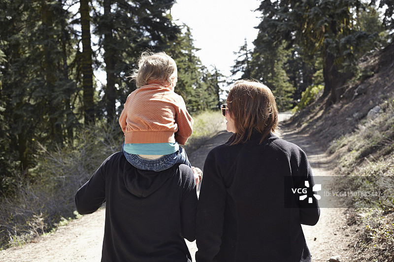 美国俄勒冈州，妇女带着坐在肩膀上的幼儿穿过森林图片素材